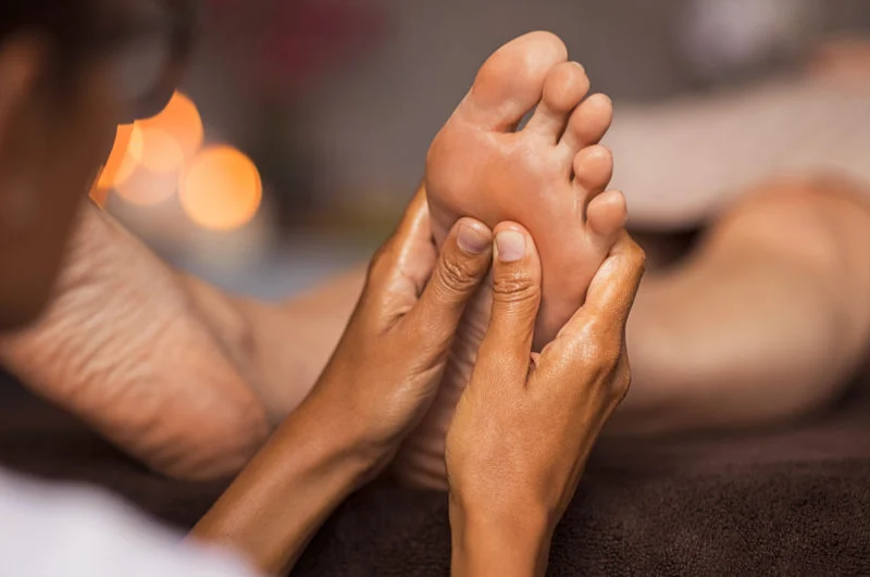 Close-up of a therapist's hands massaging and exfoliating a guest's foot in warm candlelight