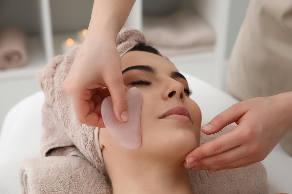 A gua sha stone gliding along a relaxed guest's cheek during a soothing face and jaw massage