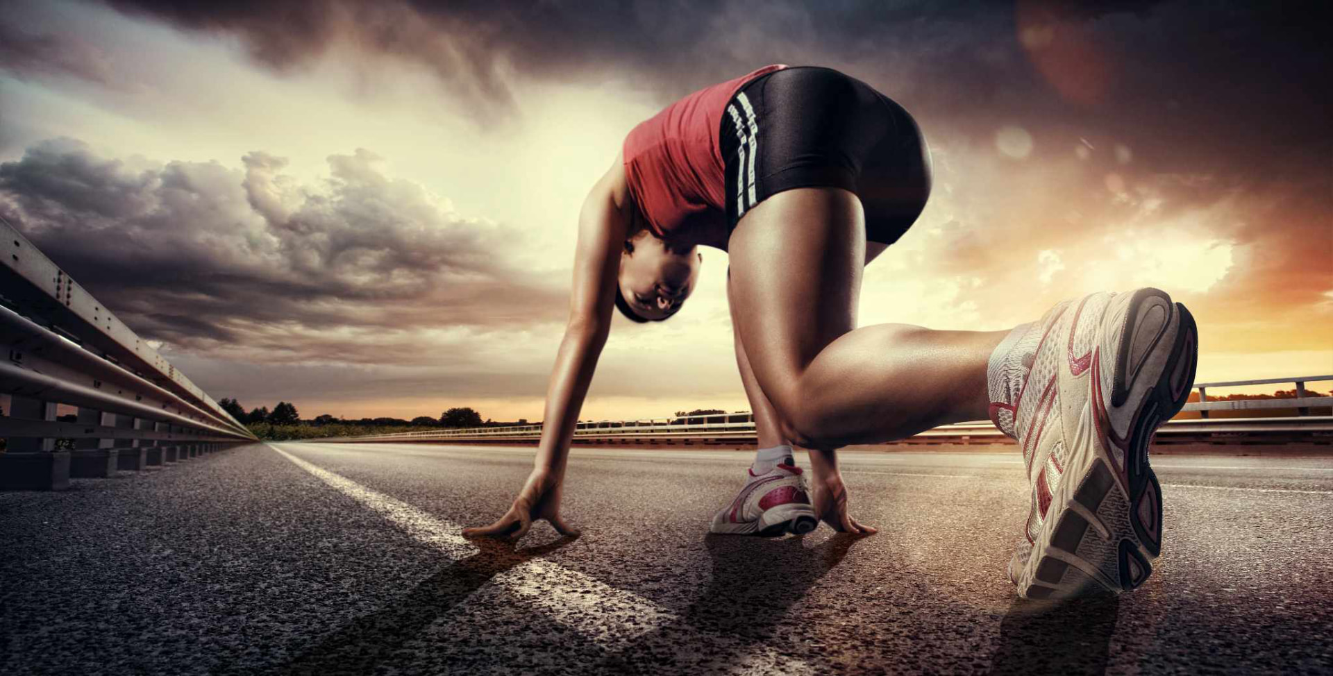 Runner in red and black athletic wear poised at the starting line on an open road at dawn, with a dramatic cloudy sky — Athens Marathon 2026
