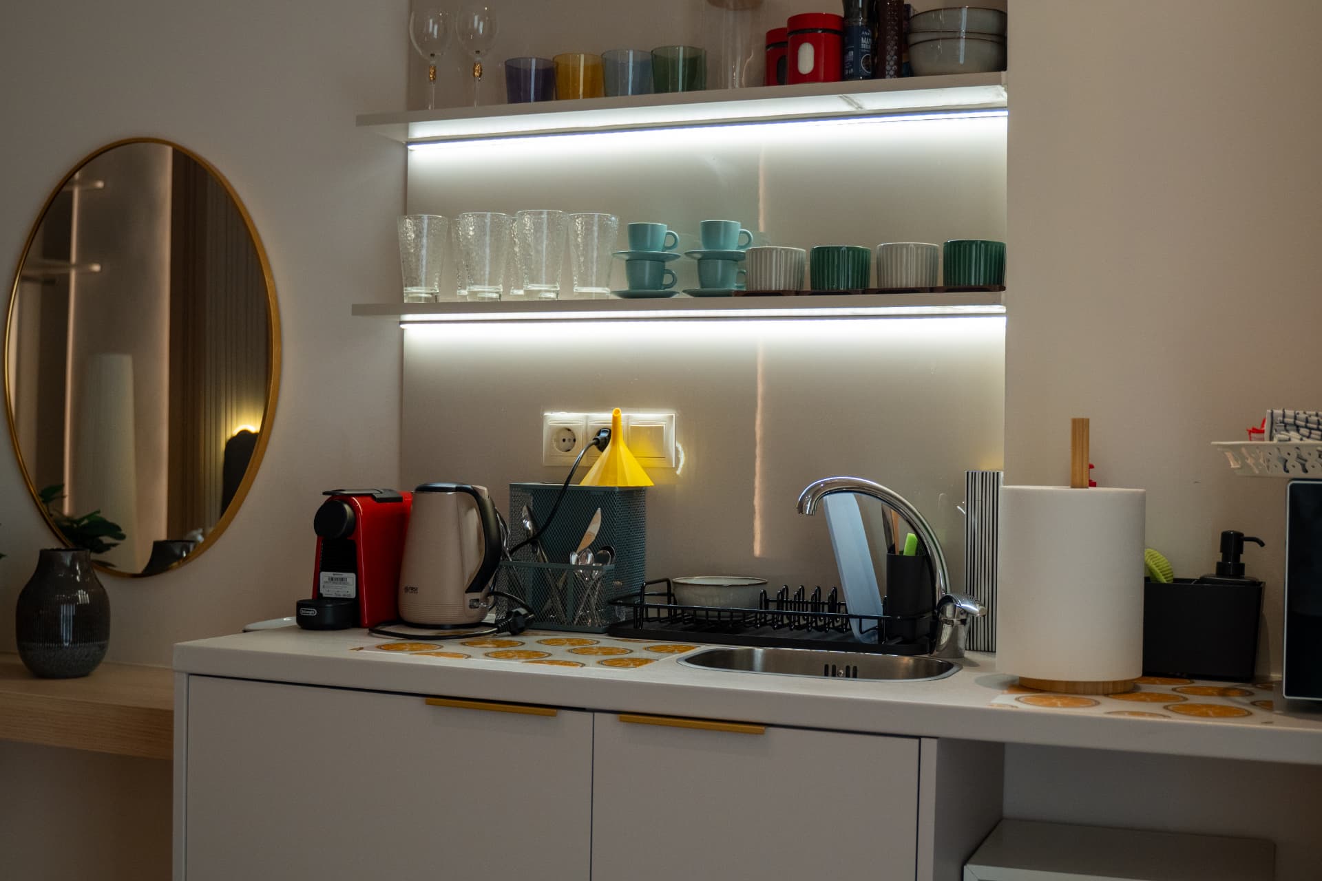 Compact suite kitchenette with a coffee maker, mugs, kettle and a round mirror above