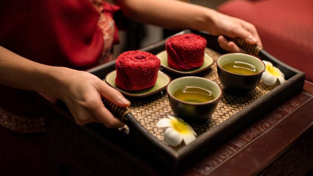 A wellness tray with herbal tea, rolled crimson towels and fresh frangipani flowers after a spa treatment