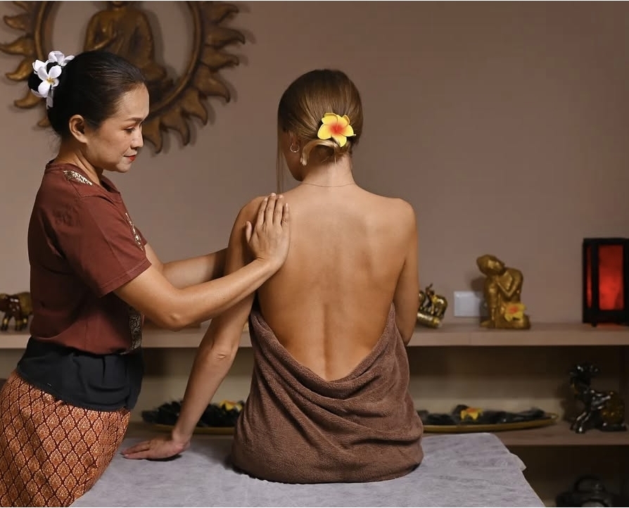 Thai therapist performing a wellness shoulder massage in a Buddha-decorated room