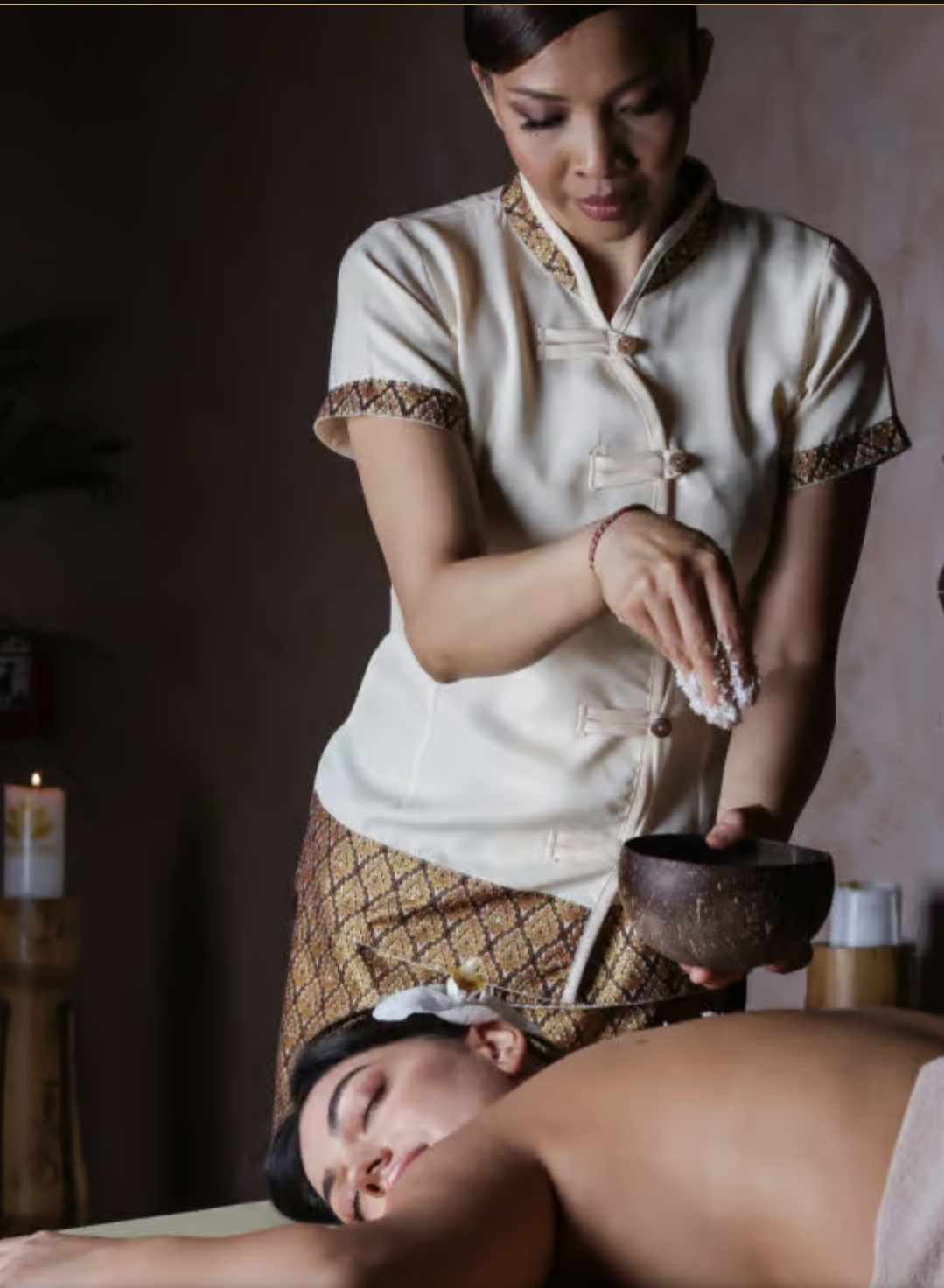A therapist applying a warm salt scrub to a relaxed guest in candlelight