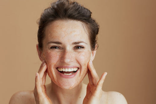 A smiling woman with a fresh sugar scrub glowing on her skin, hands resting on her cheeks, at Nuad Thai Massage Athens