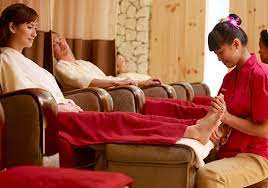 Thai therapist in red uniform massaging a guest's foot in a multi-seater foot massage parlor