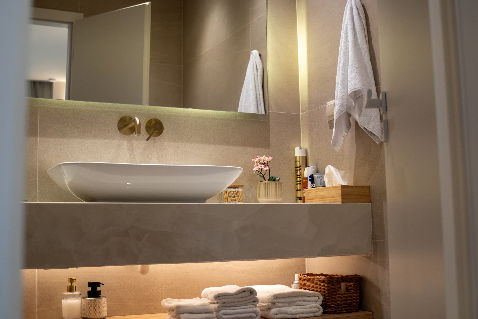 Modern en-suite bathroom with a white vessel sink, brass fixtures and stacked fresh towels