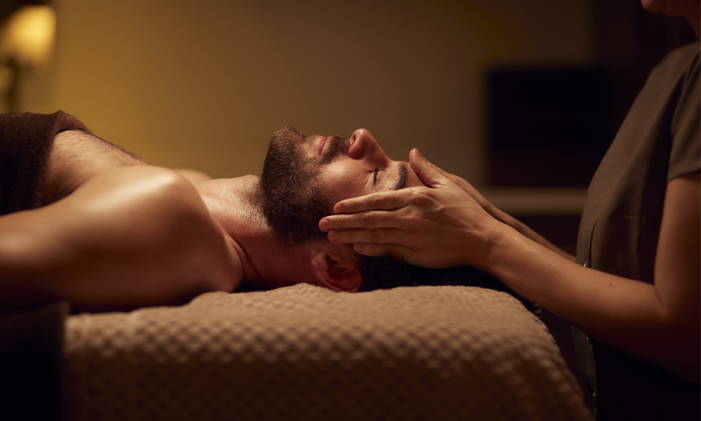 Guest lying back on a spa table while a therapist's hands rest on his temples during Jet Lag & Travel Therapy
