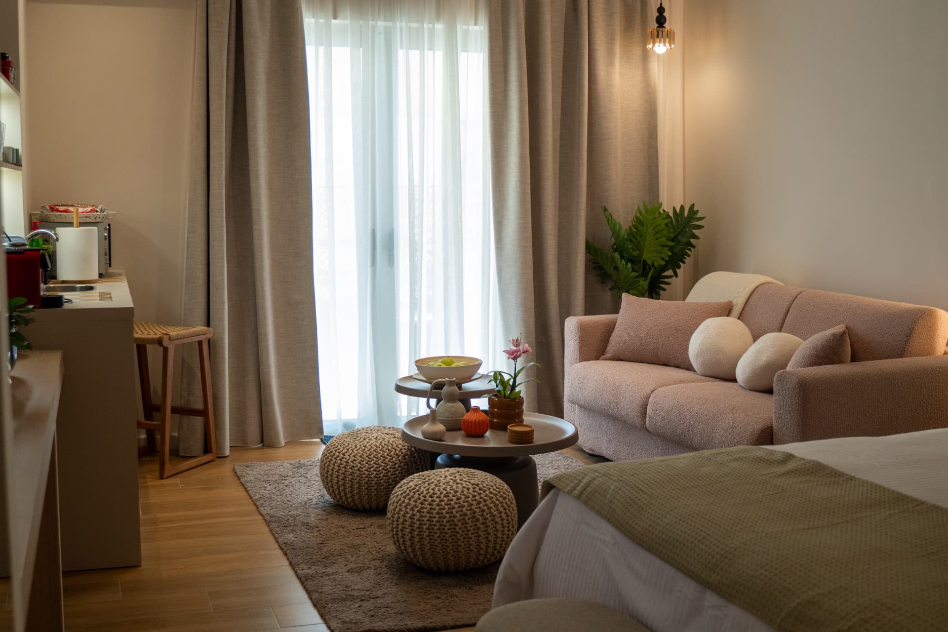 Cozy retreat suite corner with a pink sofa, woven poufs and balcony curtains filtering daylight