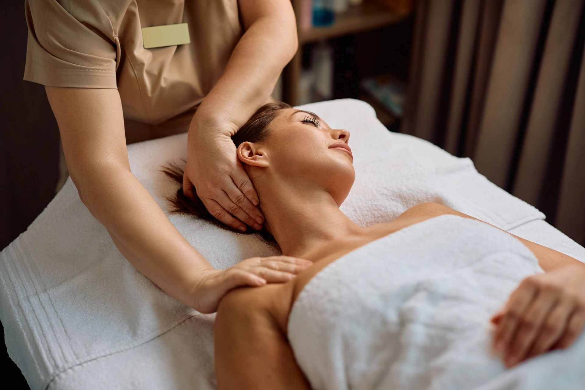 Therapist massaging a relaxed guest's neck, shoulders and upper back on a treatment table