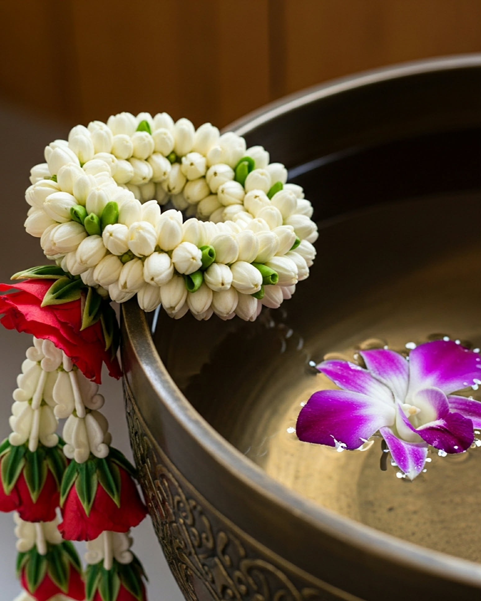 Thai jasmine garland resting on a brass bowl with a floating orchid