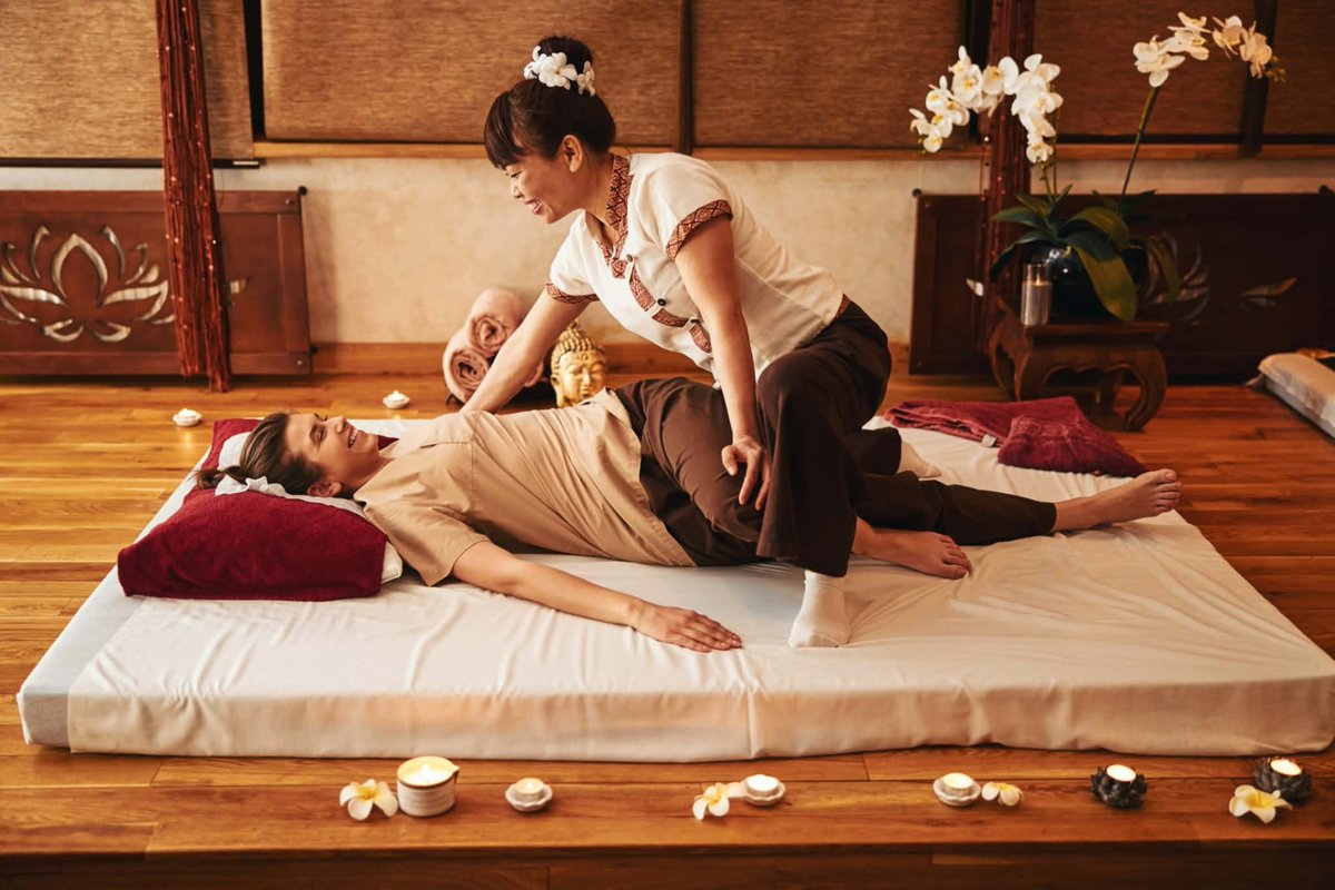 Therapist performing a traditional Thai massage leg stretch on a guest lying on a futon