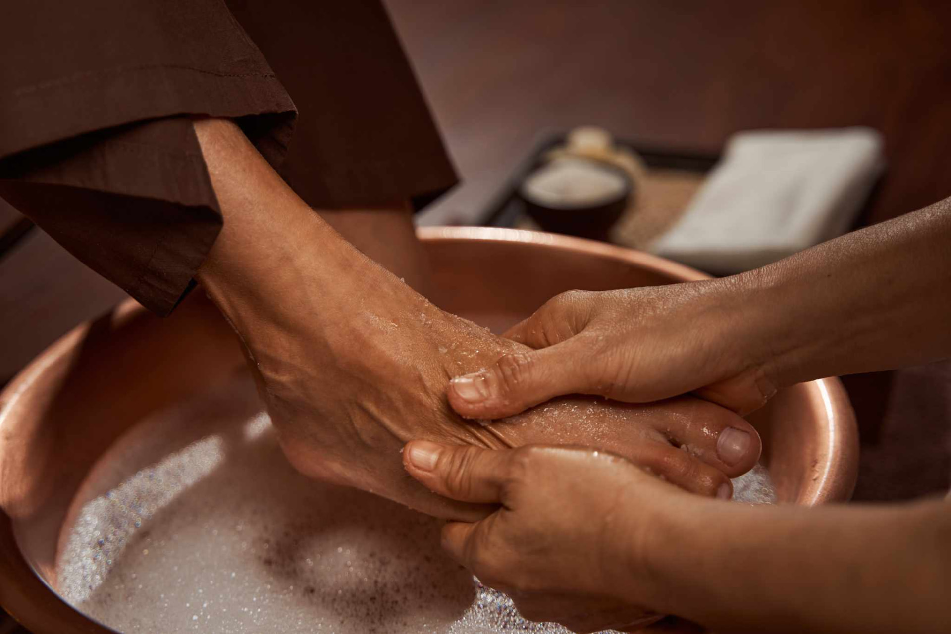 Therapist gently washing a guest's feet in a warm copper foot bath