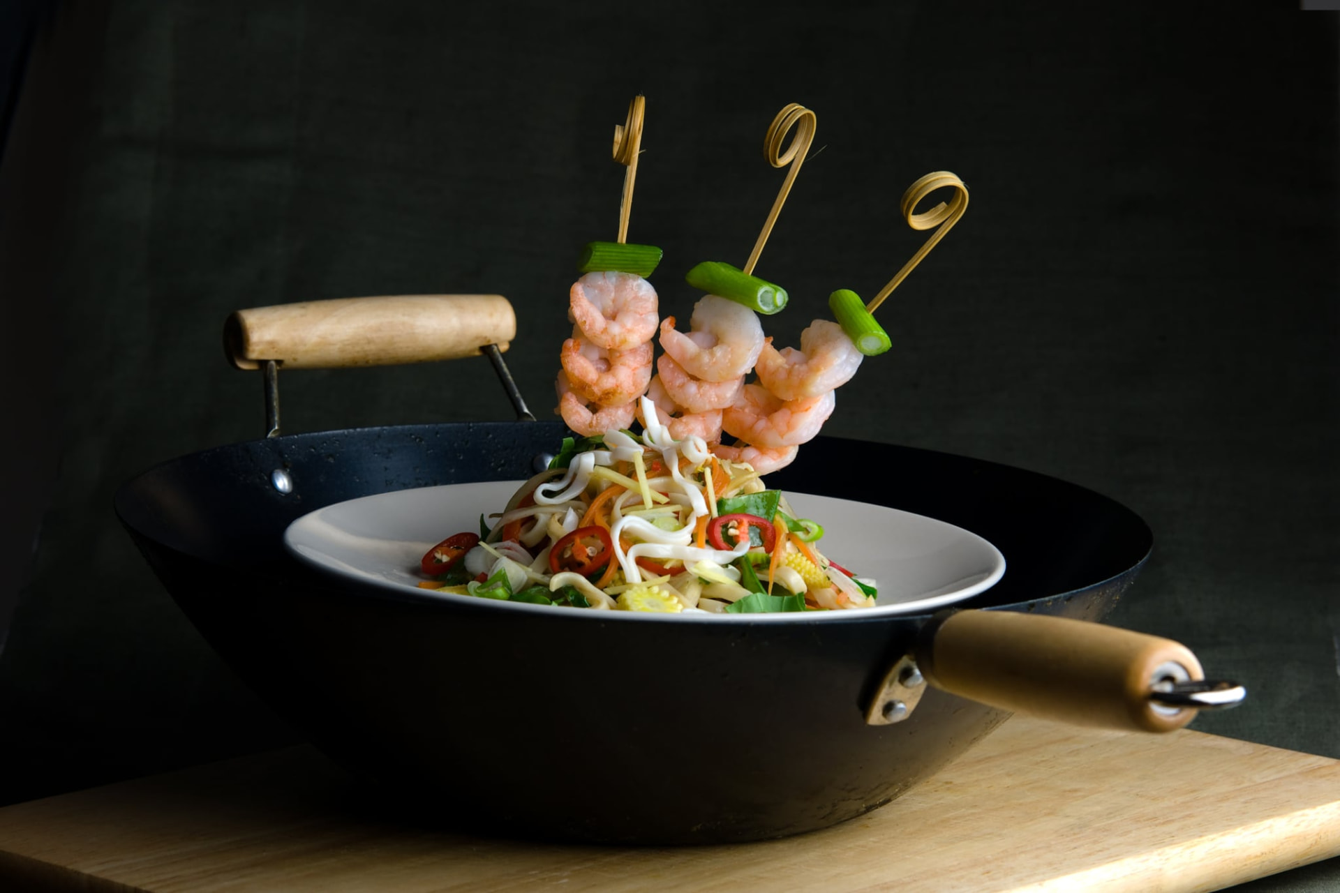 Fresh shrimp skewers over a wok-tossed noodle dish with seasonal vegetables and spring onions