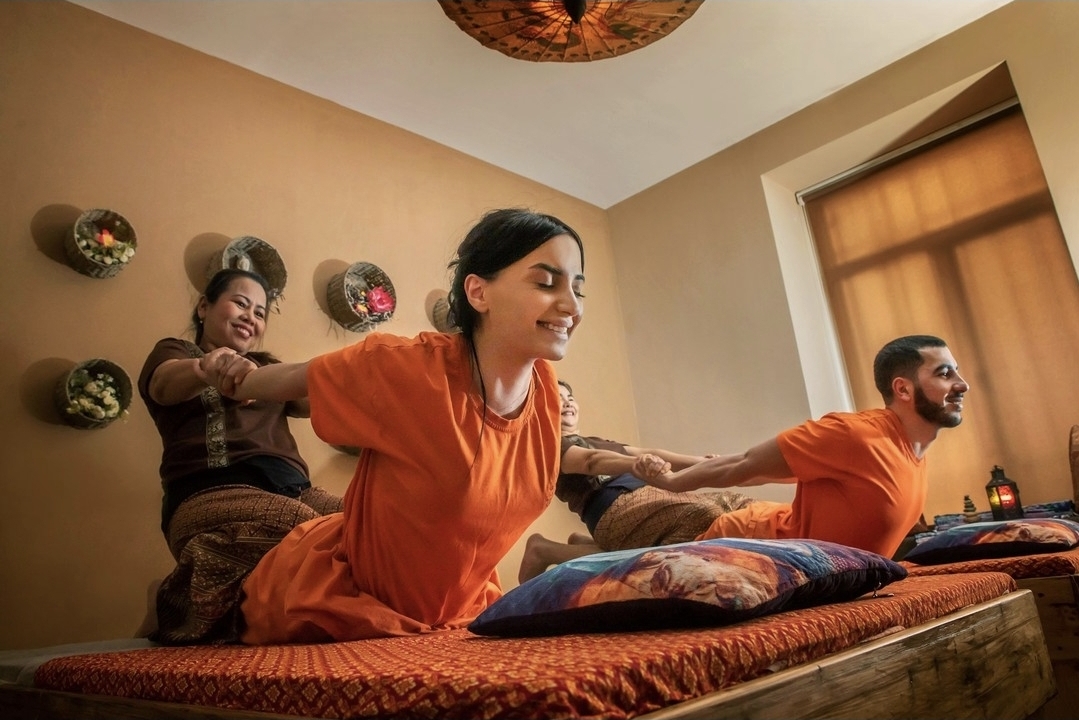 Two therapists guiding a couple through traditional Thai massage stretches on floor mattresses at Nuad Thai Massage Athens