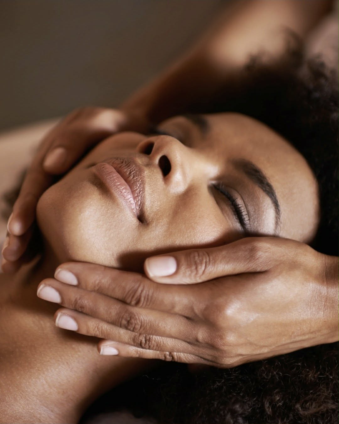 A woman with eyes closed enjoying a gentle facial massage, therapist's hands cradling her face, at Nuad Thai Massage Athens